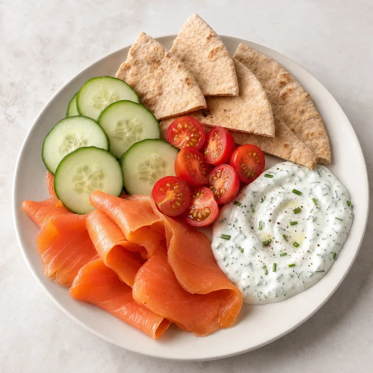 Smoked salmon breakfast plate with cucumber, tomatoes, pita, and lemon dill yogurt